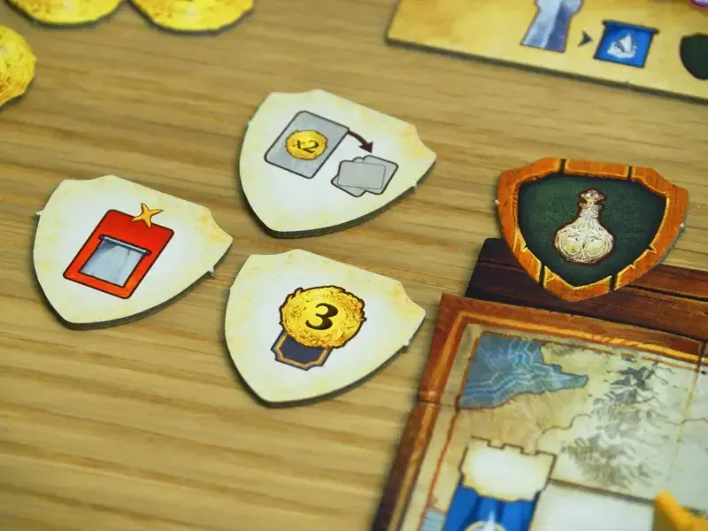 Examples of shield-shaped Alliance tokens: coins, a star marked 3 and a vial on a green field.