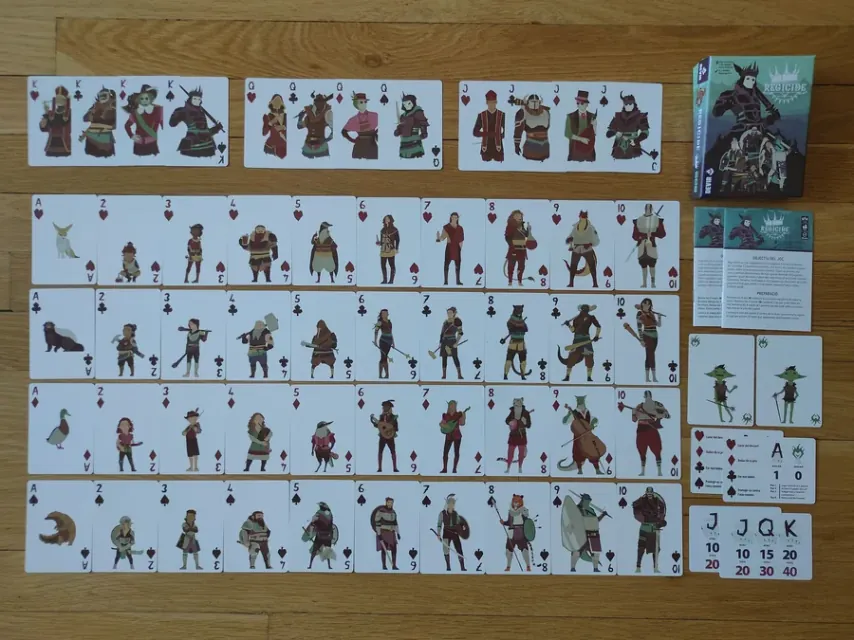 Baraja completa de Regicide extendida sobre una mesa de madera, con las cartas de números, los cuatro ases de animales y las figuras separadas arriba.