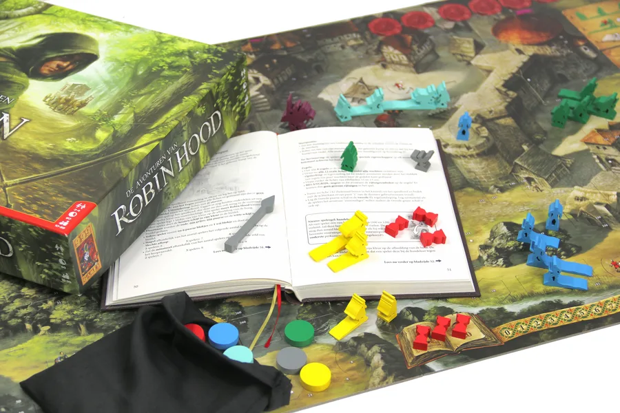 Caja de Las aventuras de Robin Hood abierta junto al libro de aventuras, el saco negro de fichas y las figuras de colores sobre el mapa.