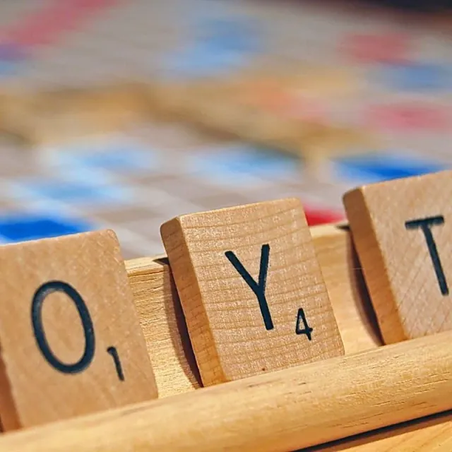 Varias fichas de Scrabble con sus valores apoyadas sobre un atril de madera.